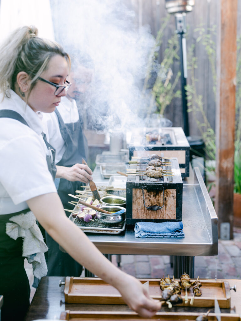 A cook grills skewers over a hot fire